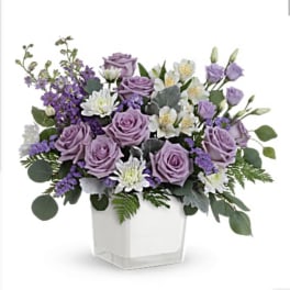 Lavender roses and white flowers in a clear square vase