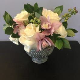 Cream roses and pink orchids arranged in a dotted glass vase