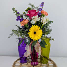 Colorful mixed bouquet in three tinted glass vases with a ribbon