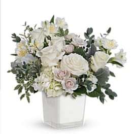 White roses and pale blooms arranged in a clear square vase