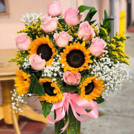 Pink roses and sunflowers arranged in a glass vase with a pink ribbon