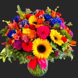 Bright mixed bouquet with sunflowers, gerbera daisies, and calla lilies in a glass vase