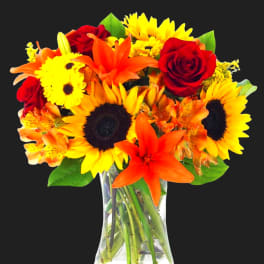 Bouquet of sunflowers, red roses, and orange lilies in a clear glass vase
