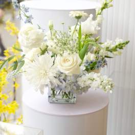 White floral arrangement in a clear square vase with blue accents