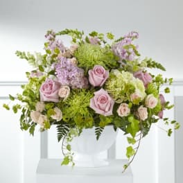 Pink roses and lavender flowers arranged in a white urn vase