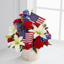 Red, white, and blue floral arrangement in a basket with small American flags