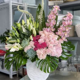 Pink and white floral arrangement in a white vase with large green leaves