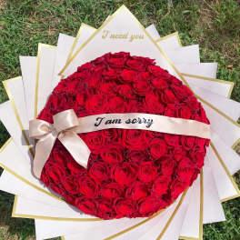 Round bouquet of red roses with a ribbon and apology message