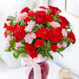 Red roses and pink carnations in a red glass vase with a pink ribbon