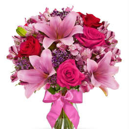 Pink lilies and roses in a glass vase with a pink ribbon