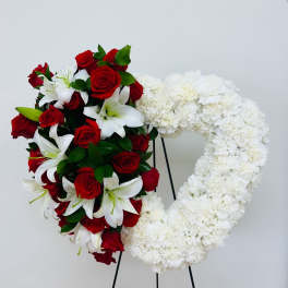 Heart-shaped floral wreath with red roses, white lilies, and white flowers on a stand