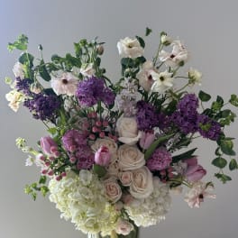 Large bouquet of pale roses, purple blooms, and white flowers in a glass vase