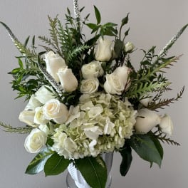 White roses and hydrangeas in a clear vase with tall greenery