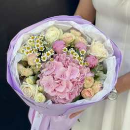 Bouquet of pink hydrangea, cream roses, and small white daisies wrapped in lavender paper