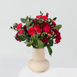 Red and pink rose bouquet in a beige vase