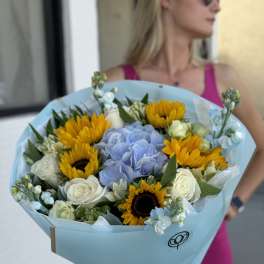 Bouquet of sunflowers, blue hydrangea, and white roses wrapped in pale blue paper