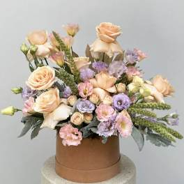 Peach and lavender floral arrangement in a round brown box