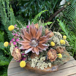 Dried floral arrangement with a large copper-toned bloom in a wooden bowl