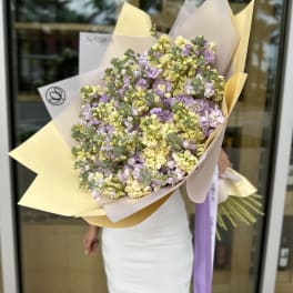 Large bouquet of pale yellow and lavender flowers wrapped in cream paper