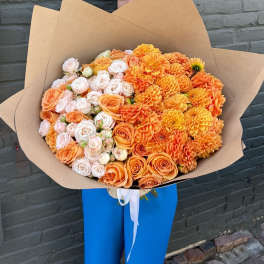 Large bouquet of orange and pale pink roses with dahlias wrapped in kraft paper