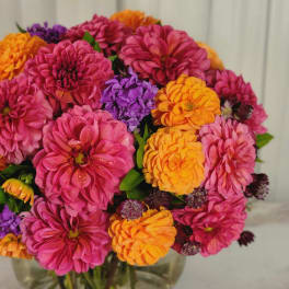 Pink, orange, and purple flowers arranged in a clear glass vase