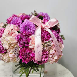 Pink and purple flower arrangement in a clear glass vase with a ribbon