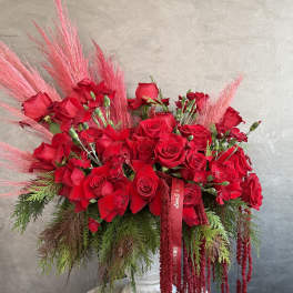 Large red rose arrangement with pink feathery accents in a white pedestal vase
