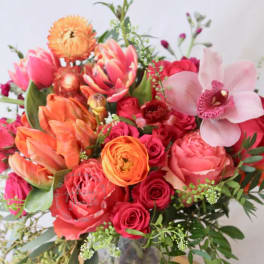 Mixed bouquet of pink, orange, and red flowers in a glass vase