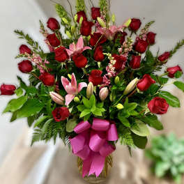 Tall arrangement of red roses and pink lilies in a glass vase with a bright pink bow