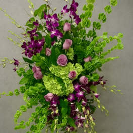 Tall standing spray of green hydrangeas, purple orchids, and pink roses on a metal easel