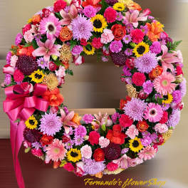 Bright circular wreath of mixed pink, yellow, and orange flowers with a large pink bow.