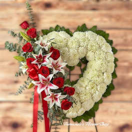 Standing heart-shaped white wreath with red roses and pink lilies on an easel with red ribbon