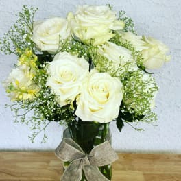 White roses arranged in a glass vase with a burlap bow