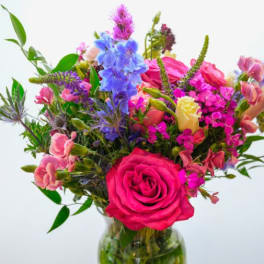 Mixed bouquet of pink, blue, and yellow flowers in a glass vase