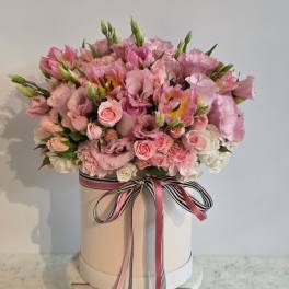 Pink floral arrangement in a round hat box with ribbon bow