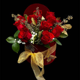 Red roses arranged in a red box with a gold ribbon