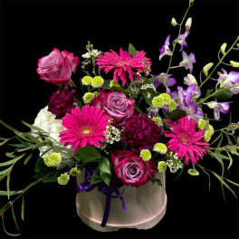 Pink roses and gerbera daisies in a white hatbox with purple ribbon