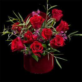 Red roses arranged in a burgundy hatbox with purple accents