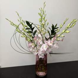 Pink orchid arrangement in a tall purple glass vase