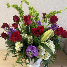 Red roses and purple blooms in a white vase
