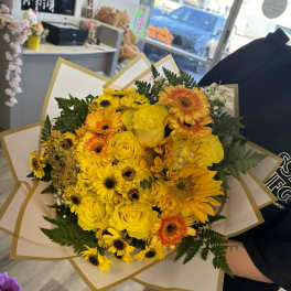 Yellow bouquet of roses and gerbera daisies wrapped in white paper