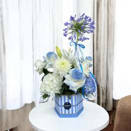 Blue and white floral arrangement in a striped box with a ribbon
