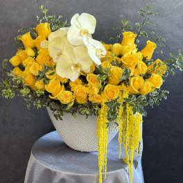 Yellow roses and white orchids in a textured white vase