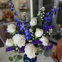 White roses and carnations with blue delphinium in a blue vase
