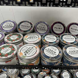Shelf of scented candles in round metal tins with assorted labels