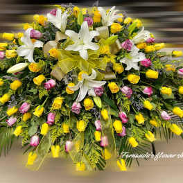 Large casket spray of yellow and pink roses with white lilies and yellow ribbon bows.