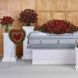 Set of red rose funeral arrangements around a silver casket, including a casket spray and heart wreath.