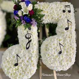 Standing floral tribute shaped like musical notes in white flowers with purple and blue accents