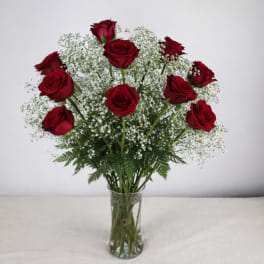 Red roses arranged in a clear glass vase with white filler flowers