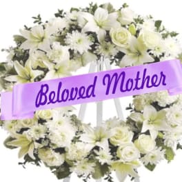 White floral wreath on an easel with a purple ribbon reading Beloved Mother